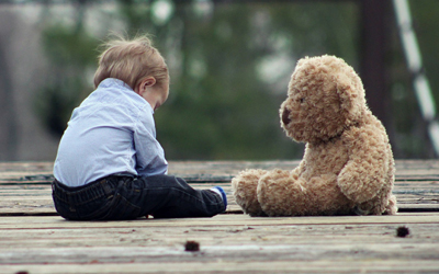 Sad child sitting alone with teddy bear